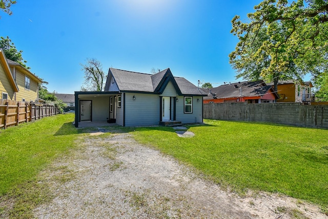 rear view of house with a lawn, a shingled roof, a fenced backyard, and driveway