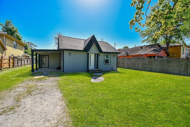 back of property featuring a fenced backyard, an attached carport, dirt driveway, a shingled roof, and a yard
