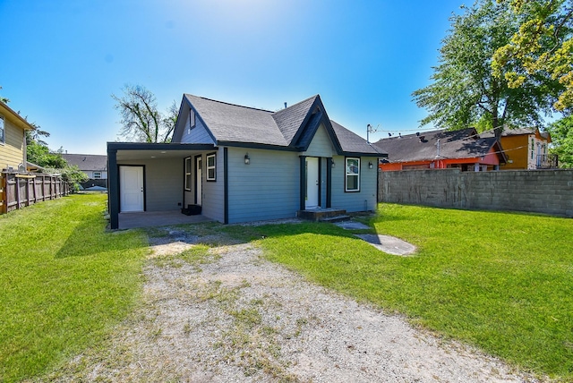 rear view of property featuring fence, a shingled roof, an attached carport, a yard, and driveway