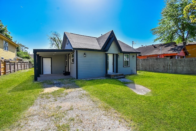 back of property with driveway, roof with shingles, a lawn, a carport, and a fenced backyard
