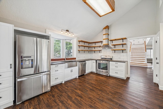 kitchen with open shelves, appliances with stainless steel finishes, dark countertops, a sink, and lofted ceiling
