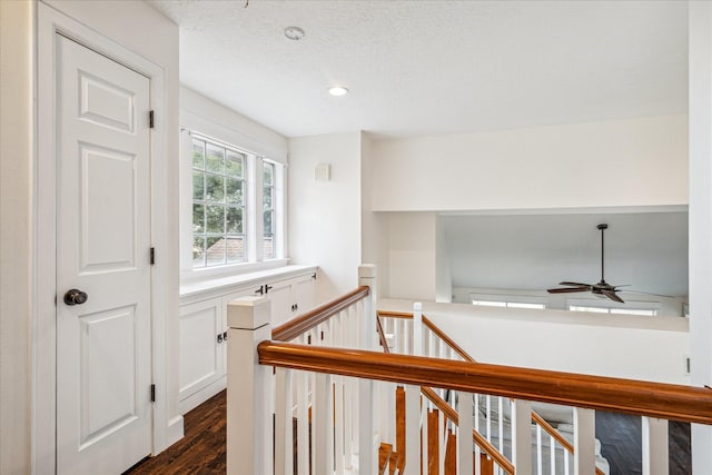 hall with dark wood-type flooring, recessed lighting, a textured ceiling, and an upstairs landing
