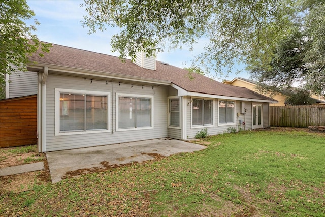back of house with a chimney, roof with shingles, a lawn, fence, and a patio
