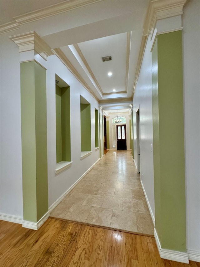 hall featuring a notable chandelier, visible vents, baseboards, and a raised ceiling