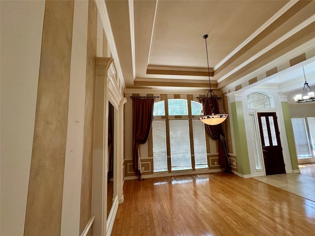 foyer entrance featuring crown molding, a notable chandelier, a raised ceiling, a decorative wall, and wood finished floors