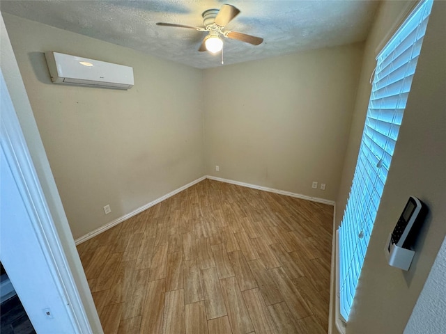 spare room featuring wood finished floors, baseboards, ceiling fan, a textured ceiling, and a wall unit AC