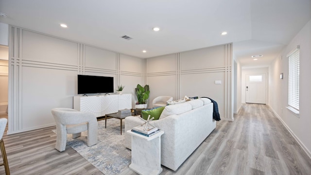 living area with recessed lighting, light wood-style floors, visible vents, and a decorative wall