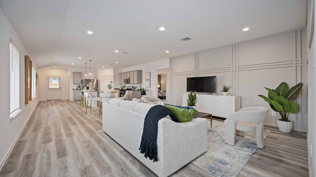 living area featuring visible vents, recessed lighting, a decorative wall, and light wood-type flooring