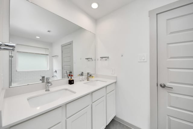 bathroom with double vanity, a sink, baseboards, and recessed lighting