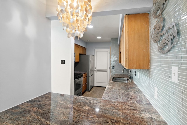 kitchen featuring brown cabinetry, electric range, dark stone counters, a sink, and backsplash