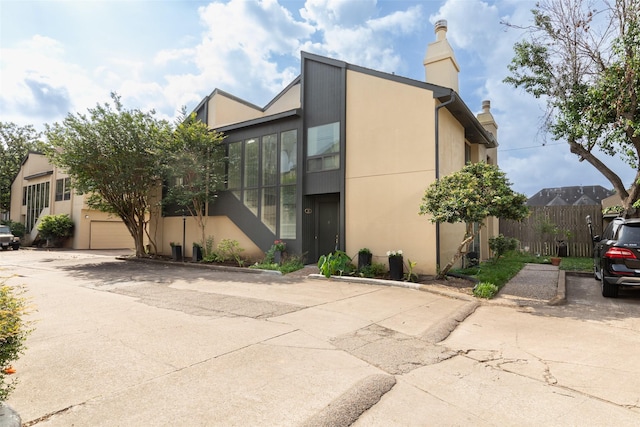 exterior space featuring stucco siding, a garage, fence, and a chimney