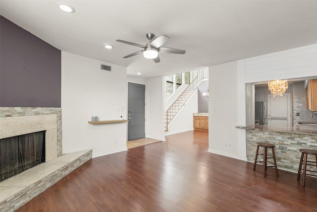unfurnished living room with visible vents, wood finished floors, ceiling fan with notable chandelier, stairs, and a premium fireplace