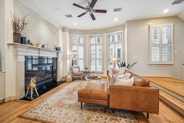 living room featuring a ceiling fan, visible vents, a glass covered fireplace, and wood finished floors