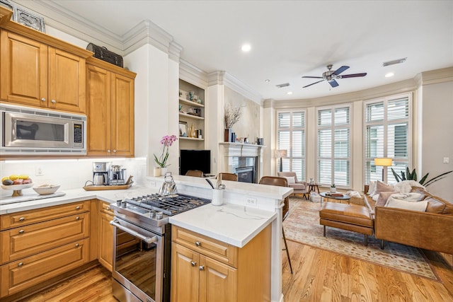 kitchen with a peninsula, open floor plan, ceiling fan, light wood finished floors, and stainless steel appliances