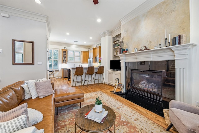 living area featuring recessed lighting, a fireplace with flush hearth, ornamental molding, and light wood-style floors