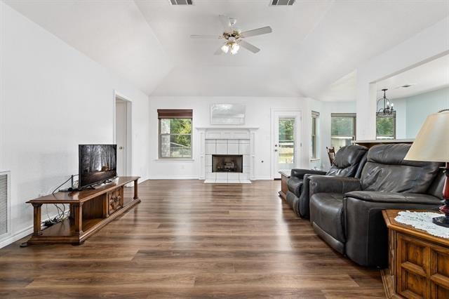 living room featuring ceiling fan, vaulted ceiling, a tiled fireplace, and dark wood-type flooring