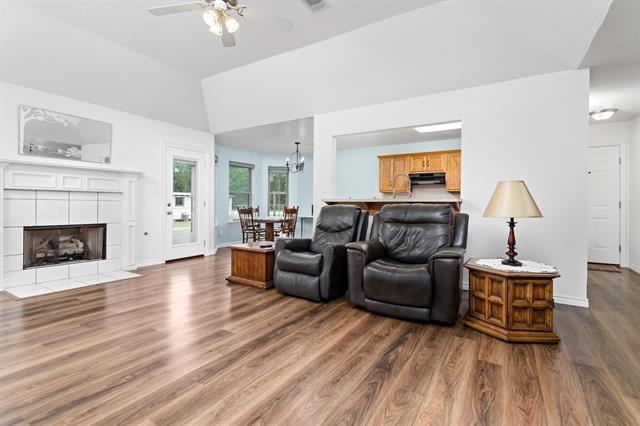 living room featuring a fireplace, ceiling fan with notable chandelier, baseboards, wood finished floors, and vaulted ceiling