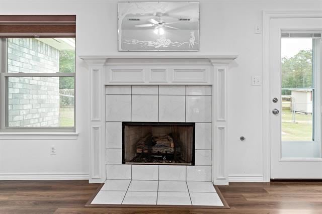 interior details featuring a ceiling fan, baseboards, a tiled fireplace, and wood finished floors
