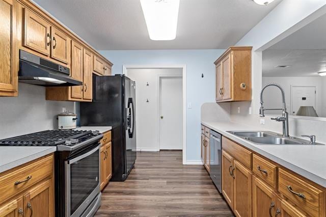 kitchen featuring dark wood-type flooring, light countertops, under cabinet range hood, a sink, and appliances with stainless steel finishes