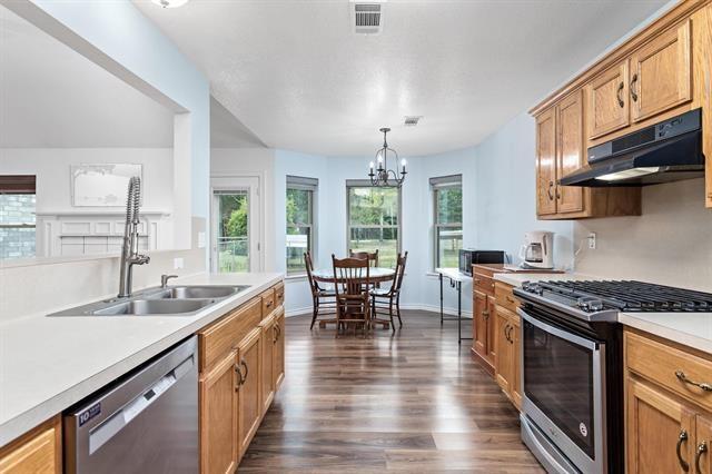 kitchen with light countertops, dark wood finished floors, stainless steel appliances, under cabinet range hood, and visible vents