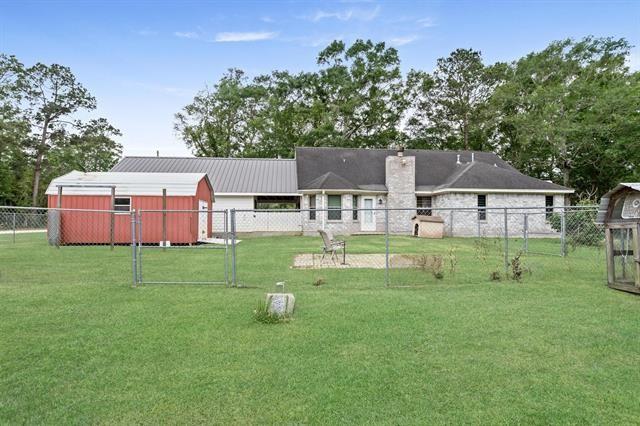 back of property with a lawn, an outdoor structure, fence, and metal roof