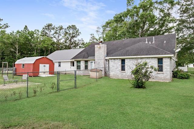 back of house with a chimney, a storage shed, a lawn, a gate, and fence