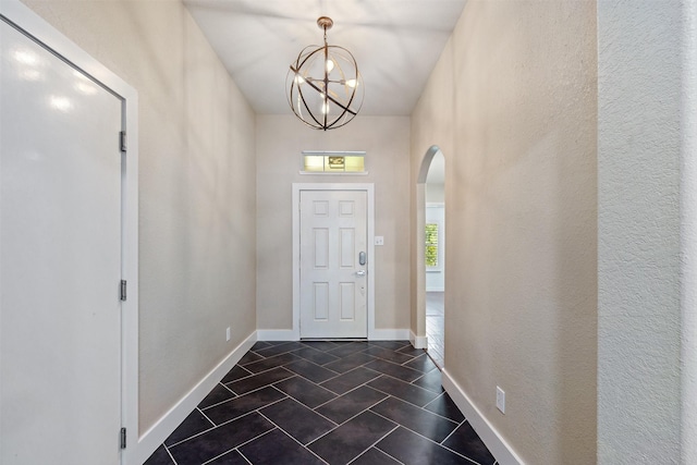 foyer with arched walkways, baseboards, dark tile patterned floors, and a chandelier