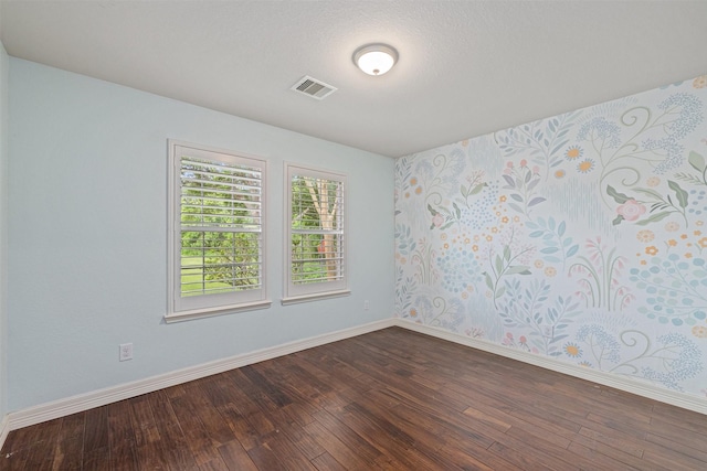 unfurnished room featuring baseboards, dark wood-style flooring, and visible vents