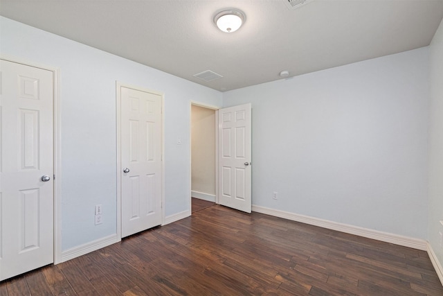 unfurnished bedroom featuring baseboards, dark wood-style flooring, and visible vents