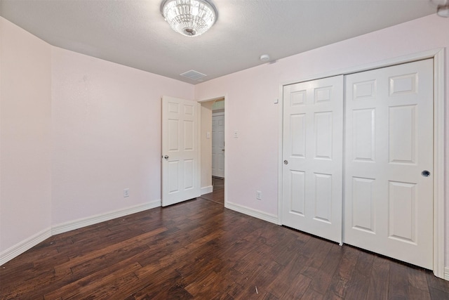 unfurnished bedroom featuring baseboards, visible vents, dark wood-style floors, and a closet