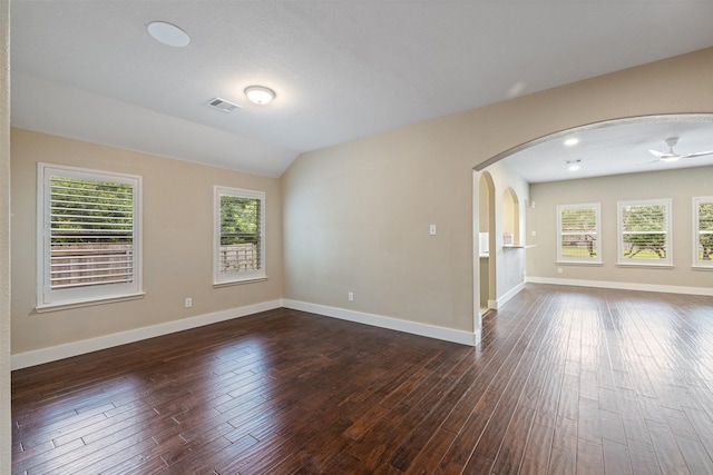 unfurnished room with arched walkways, baseboards, visible vents, and dark wood-style floors