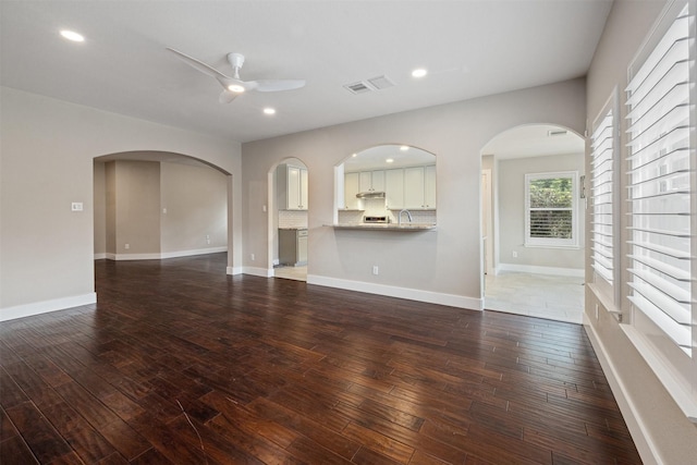 unfurnished living room featuring recessed lighting, arched walkways, a ceiling fan, and dark wood finished floors