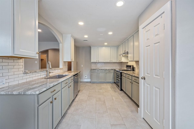 kitchen with decorative backsplash, under cabinet range hood, a sink, appliances with stainless steel finishes, and gray cabinetry