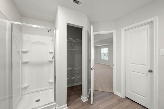 bathroom featuring a walk in closet, a shower stall, wood finished floors, and visible vents