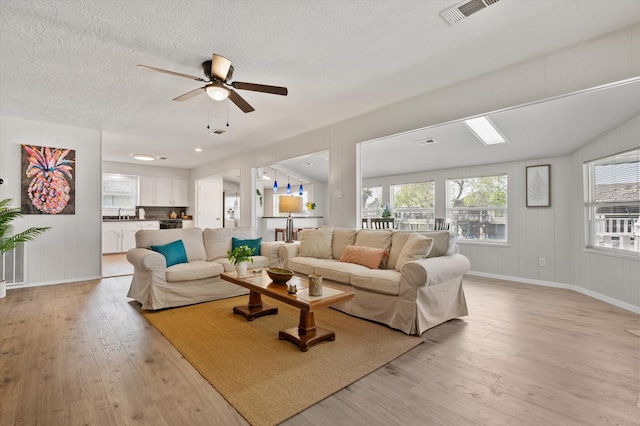 living area featuring visible vents, a ceiling fan, light wood finished floors, and baseboards
