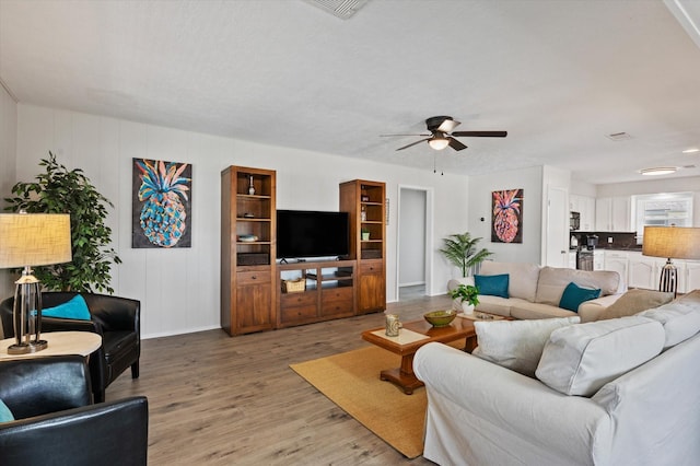 living room featuring baseboards, a ceiling fan, light wood finished floors, and visible vents