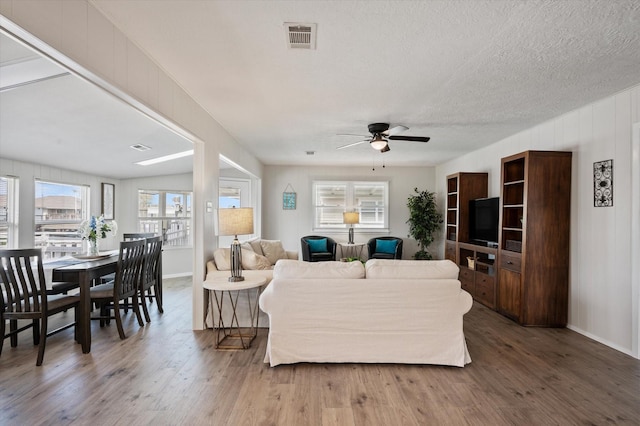 living room with a wealth of natural light, a ceiling fan, wood finished floors, and visible vents