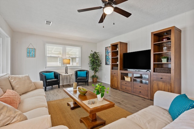 living area with a textured ceiling, ceiling fan, visible vents, and light wood-type flooring