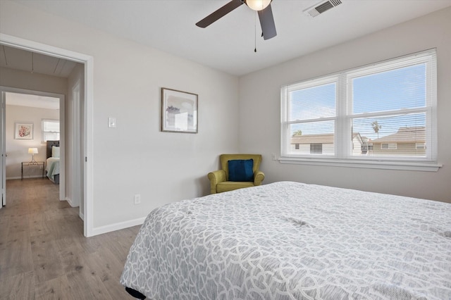 bedroom with a ceiling fan, attic access, visible vents, wood finished floors, and baseboards