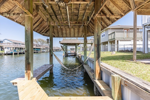 view of dock featuring a residential view, boat lift, fence, a yard, and a water view