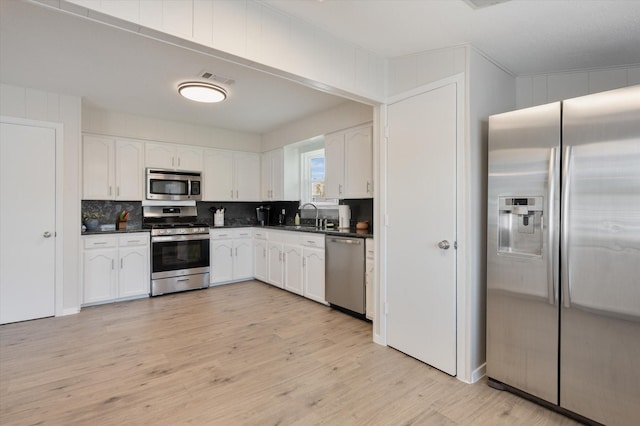 kitchen featuring white cabinetry, dark countertops, appliances with stainless steel finishes, and light wood finished floors