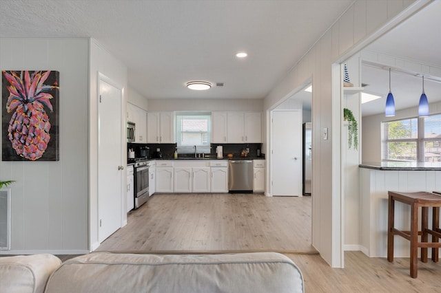 kitchen with dark countertops, light wood-type flooring, white cabinetry, a sink, and stainless steel appliances