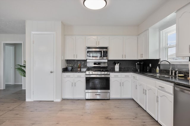 kitchen with decorative backsplash, a sink, white cabinets, light wood finished floors, and stainless steel appliances