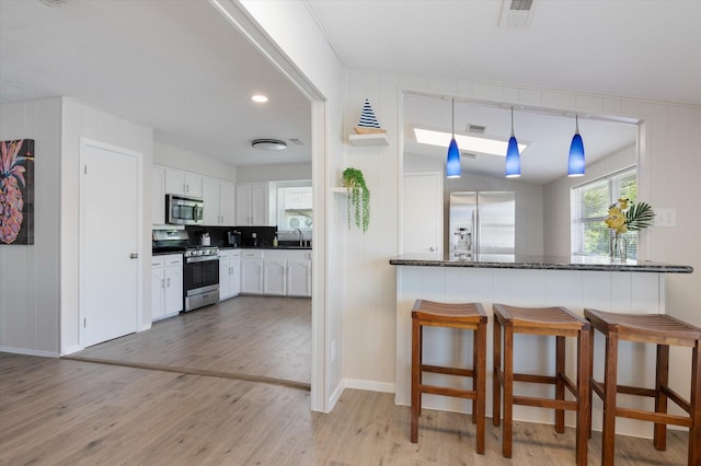 kitchen with dark countertops, appliances with stainless steel finishes, a breakfast bar area, white cabinetry, and light wood-type flooring