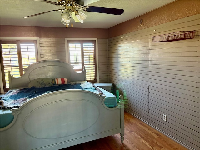 bedroom featuring wooden walls, a textured ceiling, a ceiling fan, and wood finished floors
