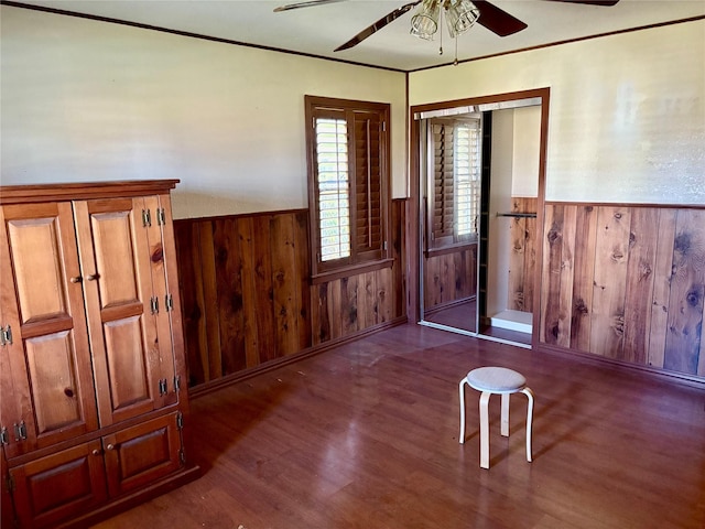 foyer entrance with wood finished floors, wood walls, a ceiling fan, and a wainscoted wall