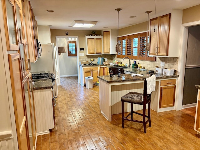 kitchen featuring a kitchen breakfast bar, tasteful backsplash, light wood-type flooring, a peninsula, and dark stone counters