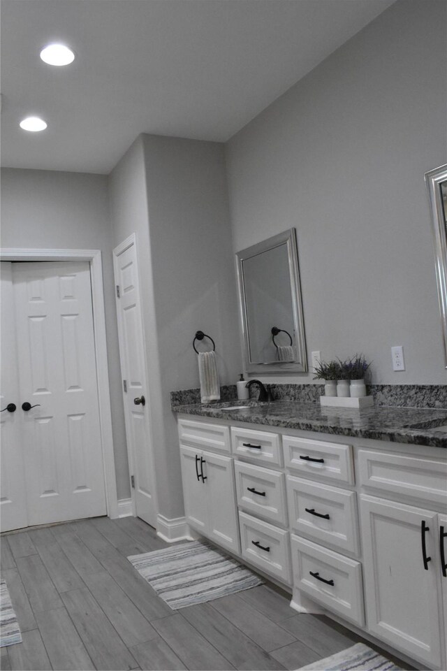 bathroom featuring double vanity, a sink, wood finished floors, and recessed lighting