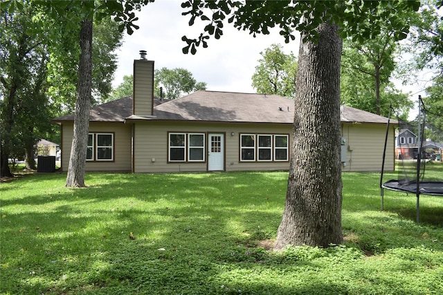 back of house featuring a yard, a chimney, and a trampoline