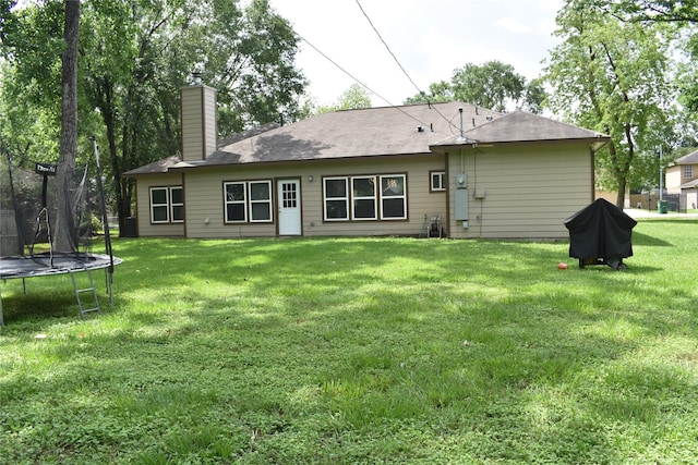 rear view of house with a lawn, a chimney, and a trampoline